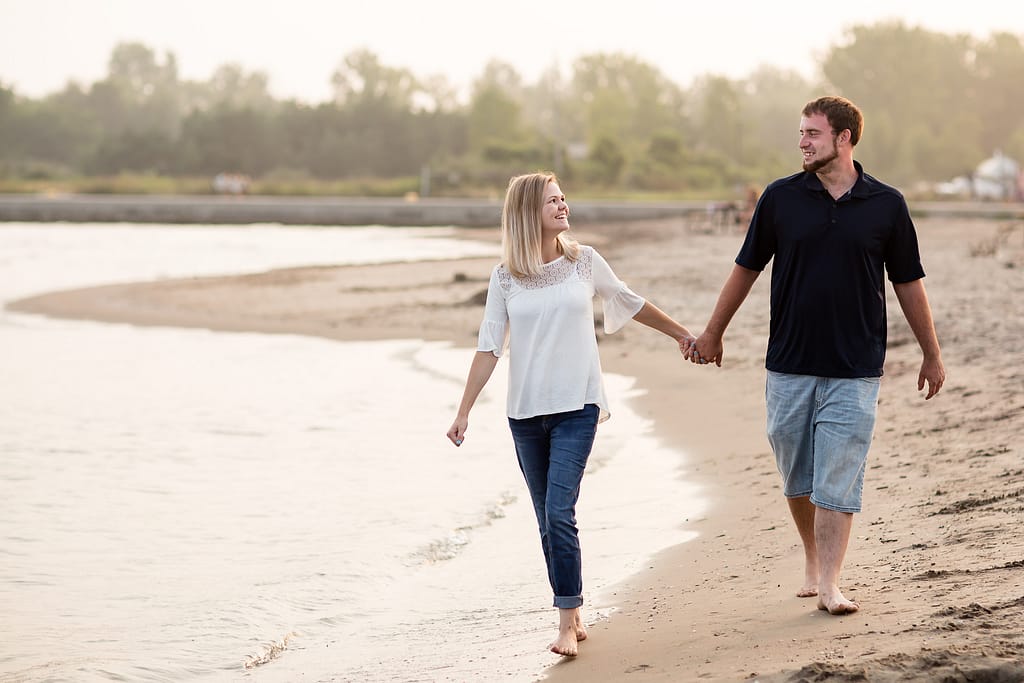 couple hold hands walking along the beach port burwell engagement photography by london ontario photographer Woodgate Photography