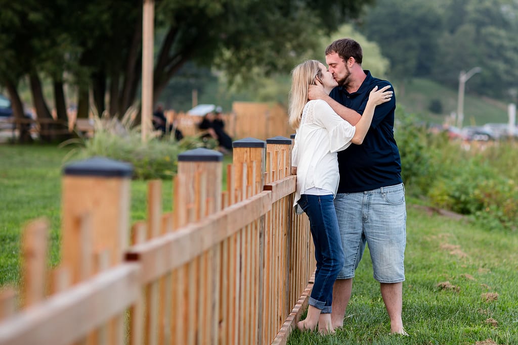 couple embrace the a fence out of focus in the foreground port burwell engagement photography by london ontario photographer Woodgate Photography